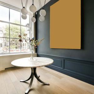 a room with blue walls and wood flooring, including a white round dining table surrounded by two hanging lamps