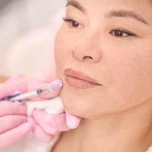 Beautiful woman undergoing injection rejuvenation procedure in a cosmetology salon, a specialist works in pink protective gloves