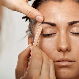 A close-up view of a makeup artist skillfully applying an eyebrow pencil to a woman's face.