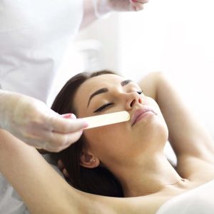 Unrecognizable crop cosmetologist applying gel on face of young woman in beauty salon