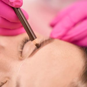 Marking the clients eyebrows before the procedure, the master works in pink gloves