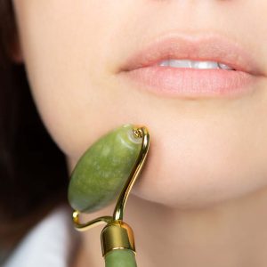 Close up of young woman with jade face roller. She is doing beauty facial massage therapy